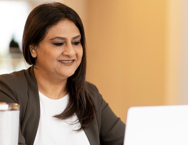 An image showing a woman with long dark hair looking at a laptop screen and typing.