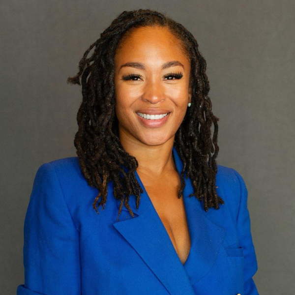 Candi Jones, blue suit, smiling, long locs.